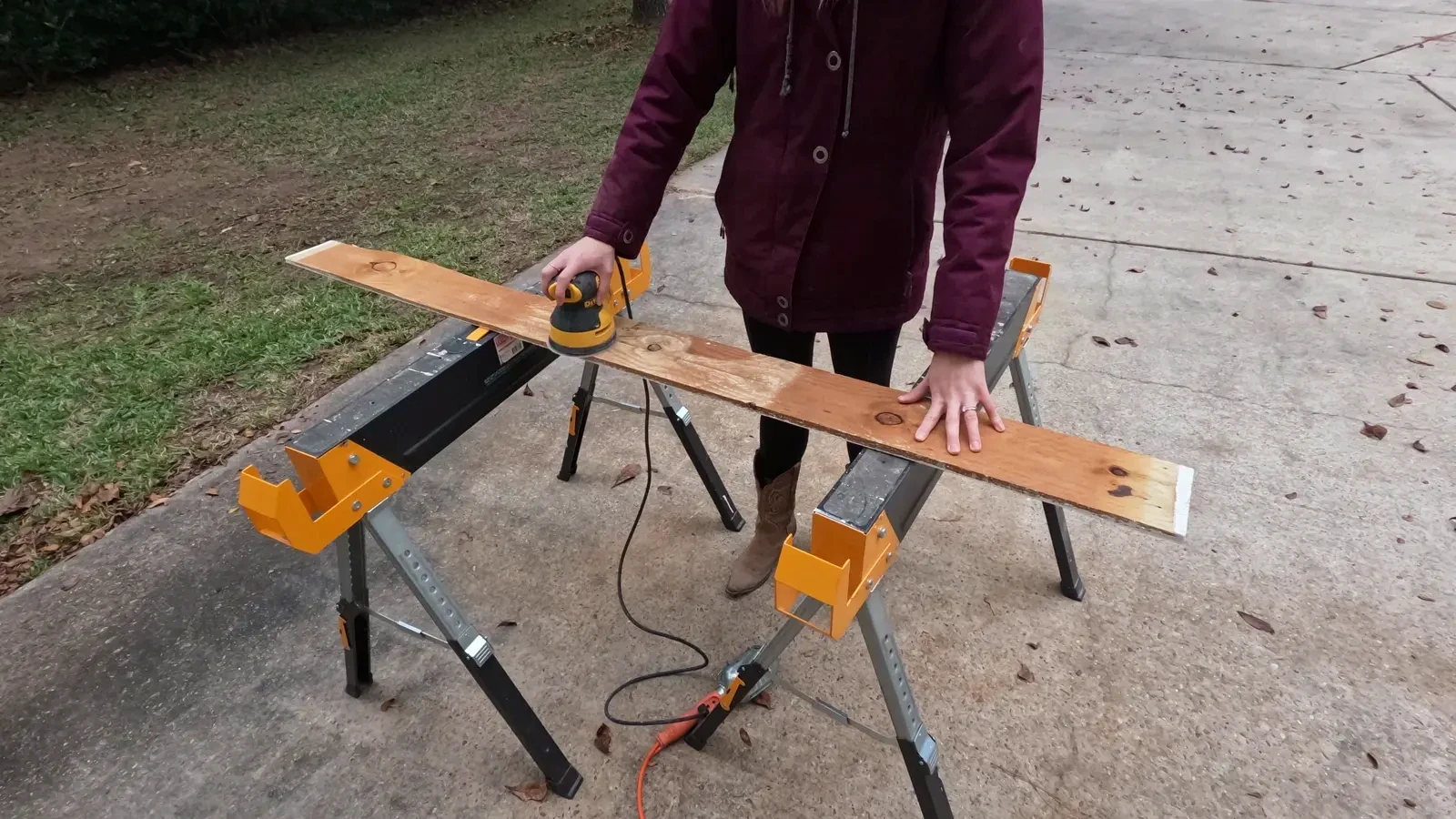 Person using a DeWalt orbital sander on the pallet wood to remove paint and smooth the surface.