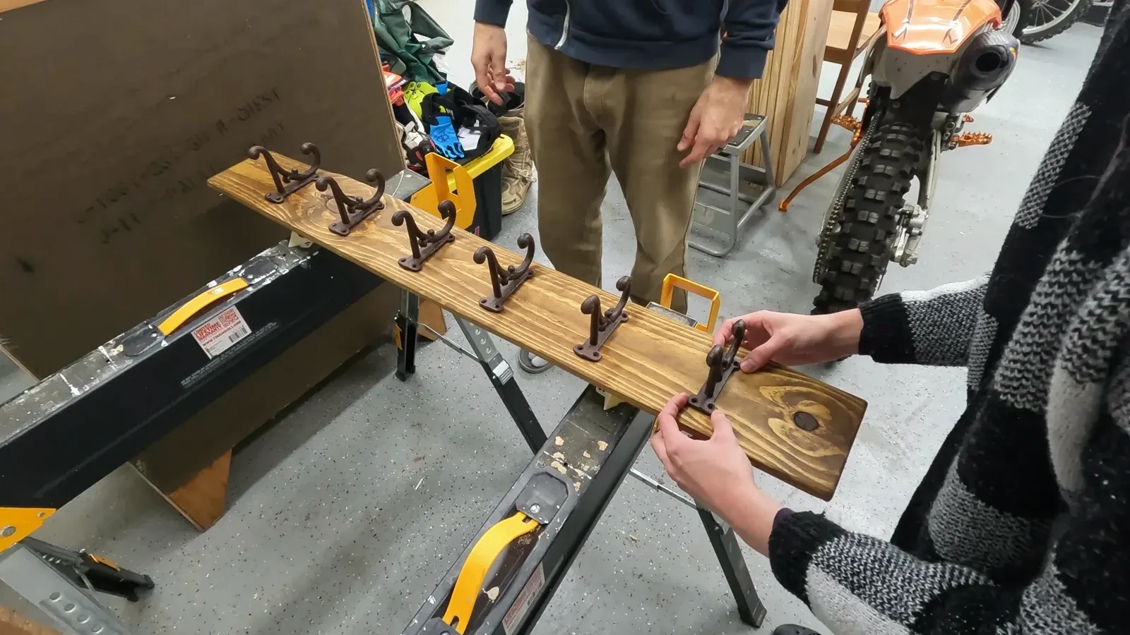 Arranging six black cast iron coat hooks on the stained wood plank to determine optimal spacing.