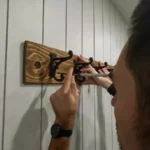 Finished rustic coat rack with six black cast iron hooks mounted on a stained wood plank, installed on a shiplap wall in a mudroom.