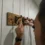 Finished rustic coat rack with six black cast iron hooks mounted on a stained wood plank, installed on a shiplap wall in a mudroom.
