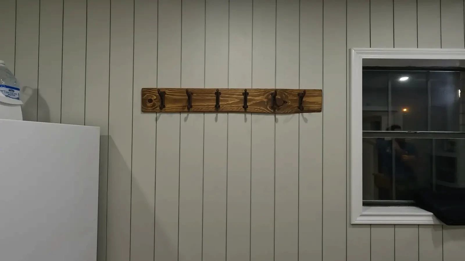 Close-up of the installed rustic coat rack, showing the texture of the wood, the cast iron hooks, and a coat hanging on one of the hooks.