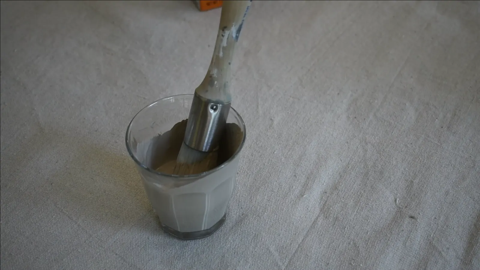 Mixing beige paint with white baking soda in a plastic cup to create a thick, textured mixture.