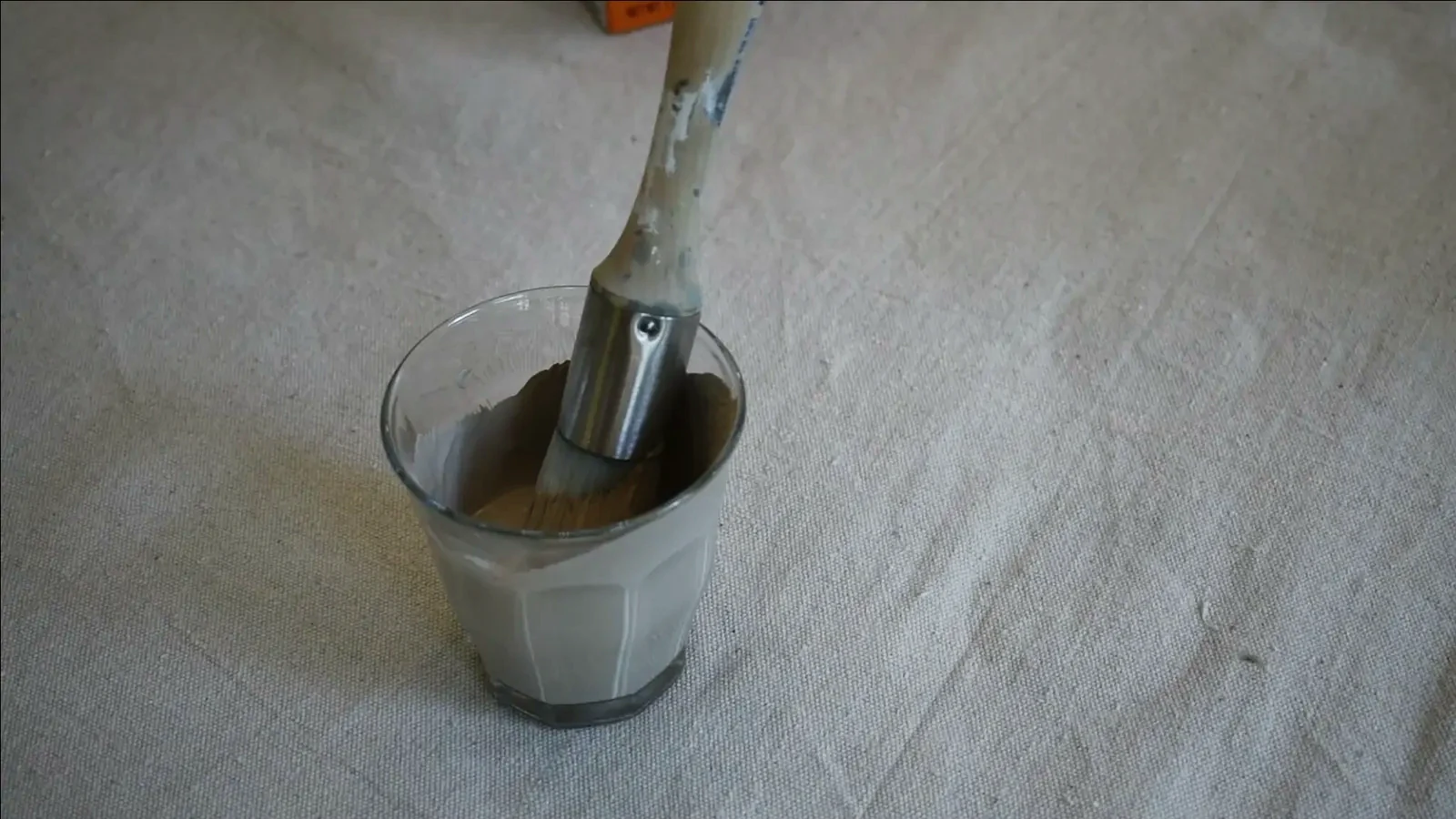 A close-up of a paintbrush applying the textured paint and baking soda mixture to a glass vase.